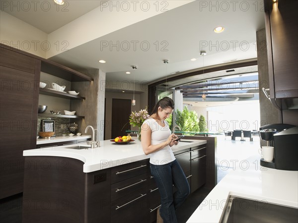 Young woman text-messaging in her kitchen.