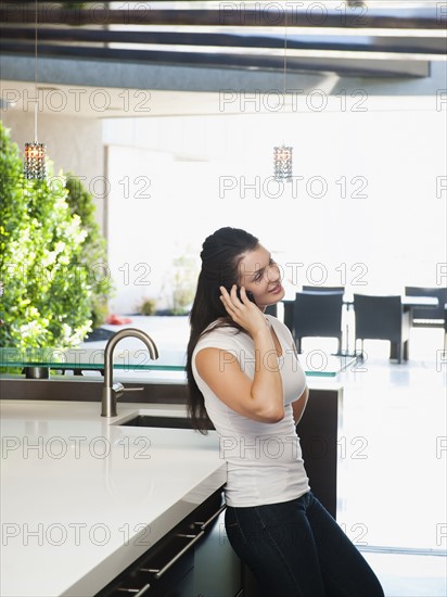 Young woman using mobile phone in her kitchen.