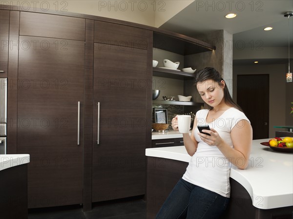 Young attractive woman enjoying morning cup of coffee while checking messages on her mobile phone.