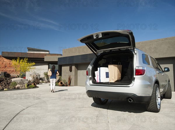 Young woman unpacking shopping from car parked in yard.