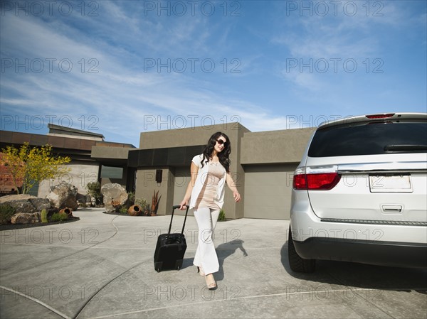 Young woman with suitcase walking towards car.
