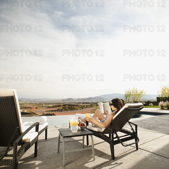 Young attractive woman reading book by swimming pool.