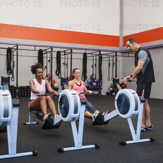 Two women exercising in gym supervised by their trainer.