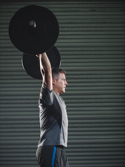 Mature man lifting heavy barbell .