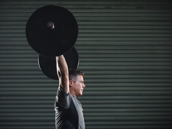 Mature man lifting heavy barbell .