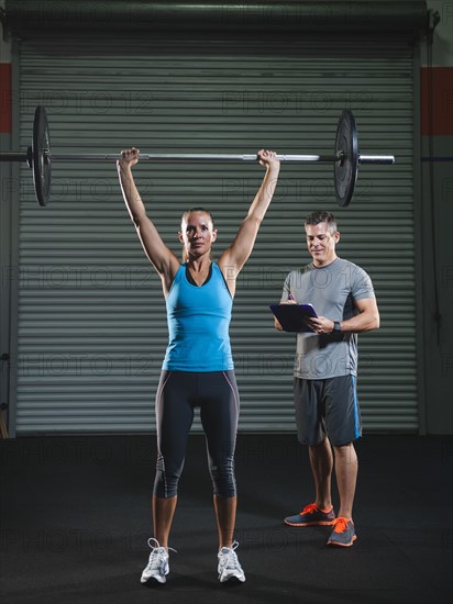 woman lifting barbell supervised with her trainer.