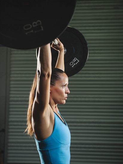 Mid adult woman lifting barbell .