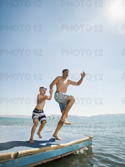 Father and son (4-5) jumping into lake caught.