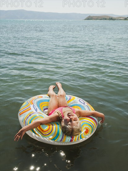 Girl (4-5) floating on water on inflatable ring and laughing.