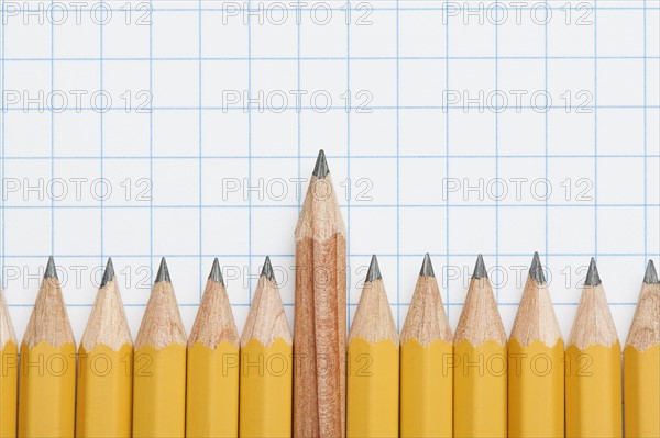 Single wooden pencil rising above row of sharpened pencils on graph paper, studio shot. Photo : Kristin Duvall