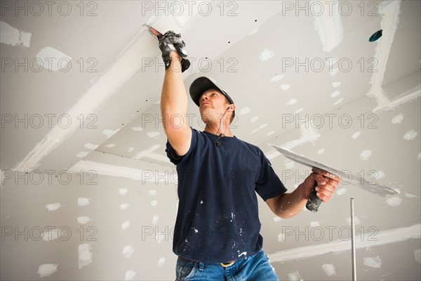 Drywall worker taping and mudding joint in ceiling. Photo : Mike Kemp