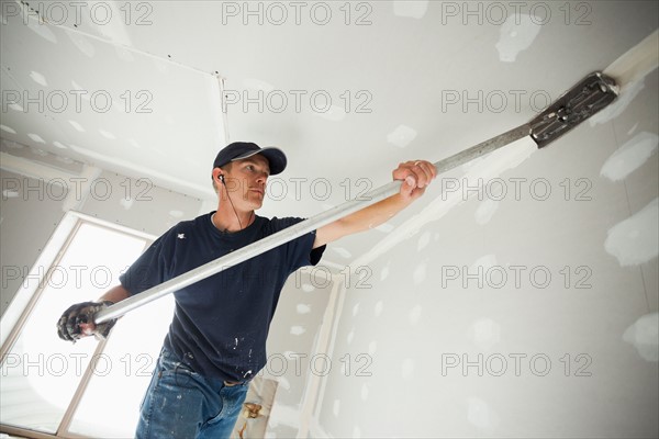 Drywall worker applying tape to corner between wall and ceiling. Photo : Mike Kemp