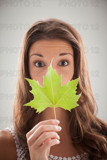 Beautiful woman holding green sycamore leaf in front of mouth and nose. Photo : Mike Kemp