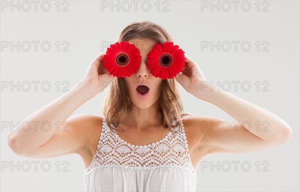 Beautiful woman holding two flowers in front of her eyes. Photo : Mike Kemp