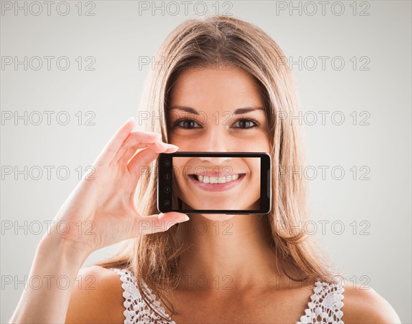 Woman smiling with smart phone in front of mouth, smile showing on screen of smart phone. Photo : Mike Kemp