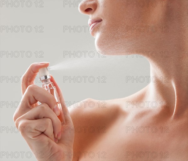 Beautiful woman spraying perfume on her neck. Photo : Mike Kemp