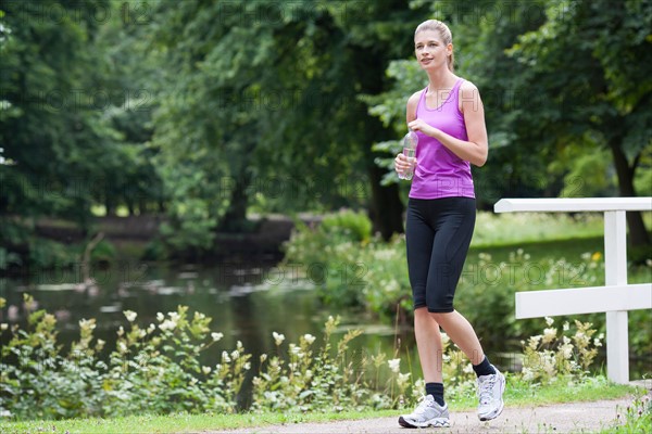 Young woman walking over a bridge with a bottle of water in her hand