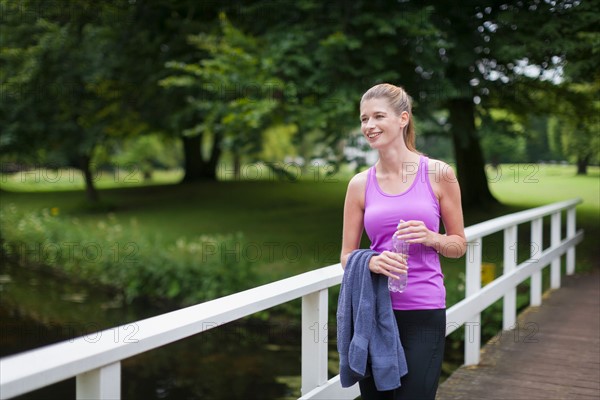 Young woman walking on a bridge after running and holding a towel and a bottle of water