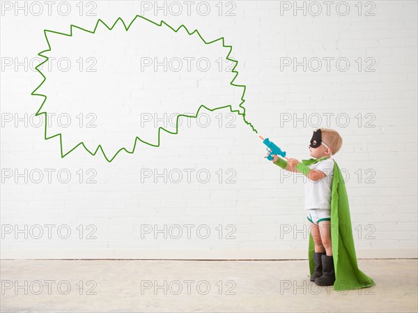 Studio shot, Portrait of boy (2-5 years) wearing green cape and holding his toy gun. Photo : Jessica Peterson