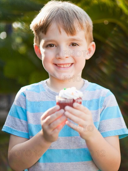 Smiling boy holding cupcake. Photo : Jessica Peterson