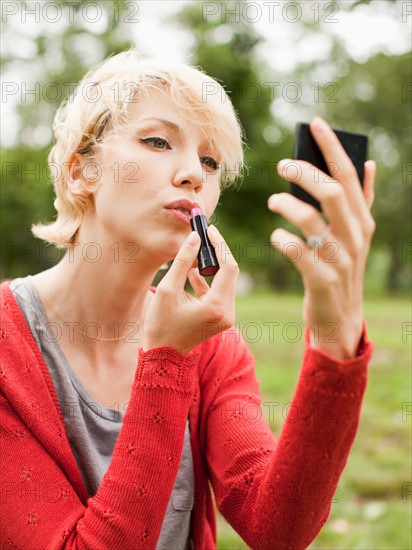 Woman holding mirror and using lipstick. Photo : Jessica Peterson