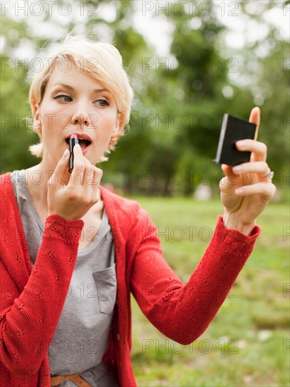 Woman holding mirror and using lipstick. Photo : Jessica Peterson