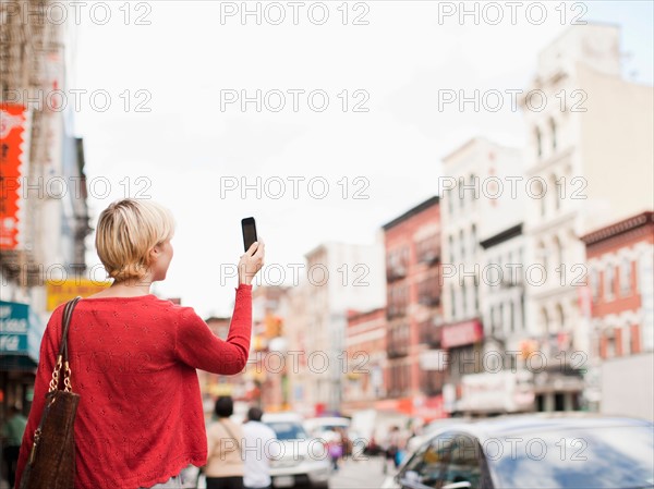 Woman taking picture with her mobile phone on street. Photo : Jessica Peterson