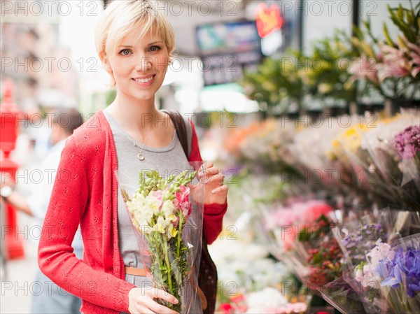 Portrait of smiling woman holding bunch of flowers outside of florist shop. Photo : Jessica Peterson