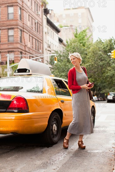 Woman standing next to yellow taxi on street. Photo : Jessica Peterson