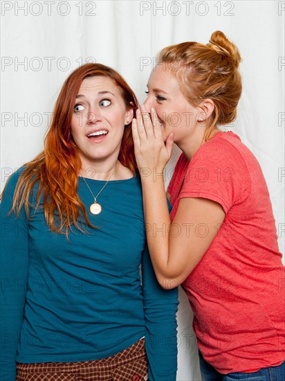 Studio Shot, Young women whispering in friend's ear. Photo: Jessica Peterson