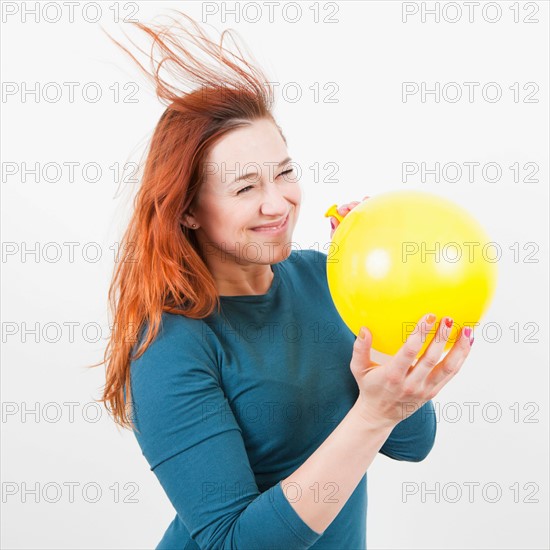 Studio Shot, Portrait of woman holding yellow balloon and letting air out of it. Photo : Jessica Peterson