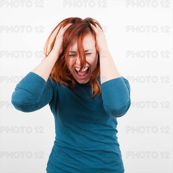 Studio shot, Portrait of woman holding her head and screaming. Photo : Jessica Peterson