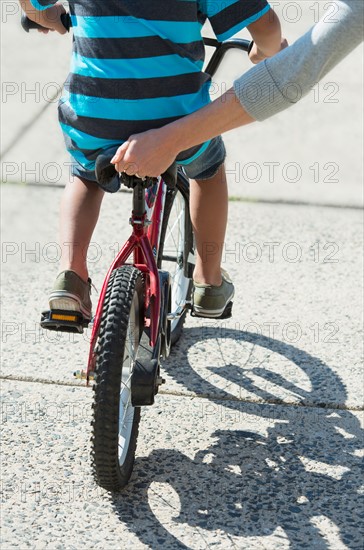 Mother helping boy (6-7) ride bicycle.