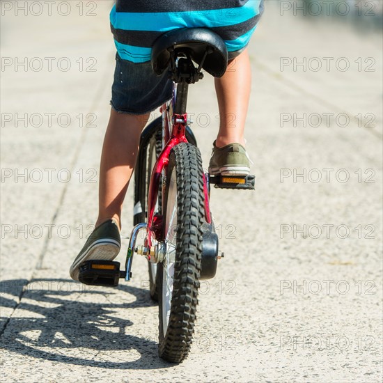 Low section of boy (6-7) riding bicycle.