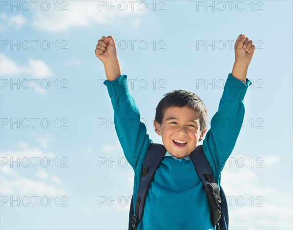 Boy (6-7) wearing backpack punching air.