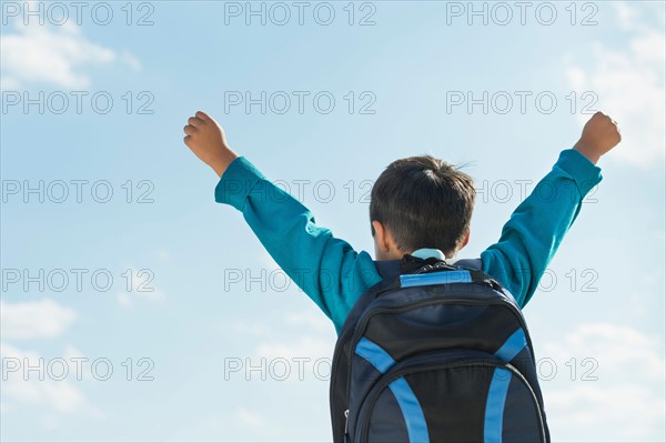 Boy (6-7) wearing backpack punching air.