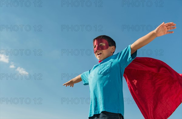 Boy (6-7) in superhero costume under blue sky.