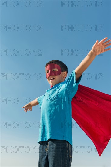 Boy (6-7) in superhero costume under blue sky.