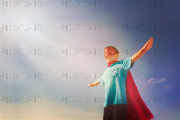 Boy (6-7) in superhero costume under blue sky.