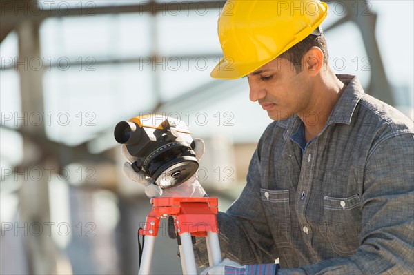 Construction worker adjusting theodolite.