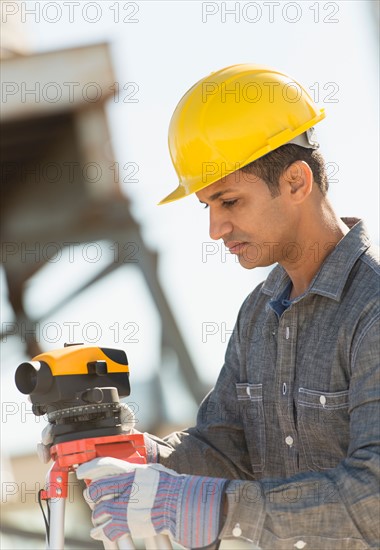 Construction worker adjusting theodolite.