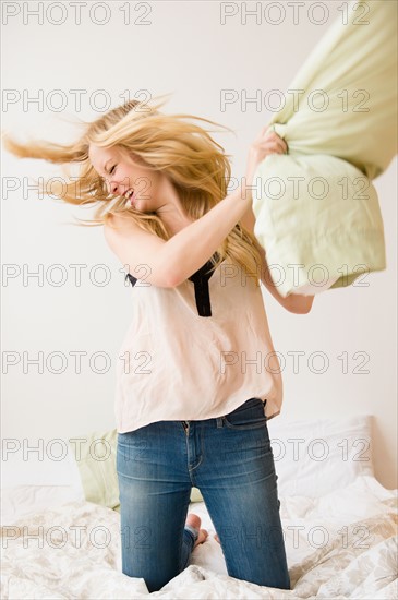 Young woman kneeling on bed and throwing pillow