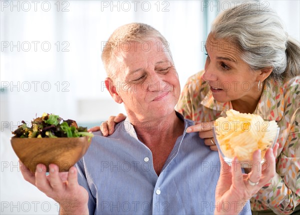 Elderly couple choosing between fresh salad and crisps