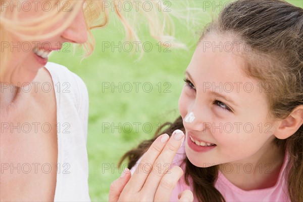 Mother applying moisturizer on daughter's (8-9 years) nose