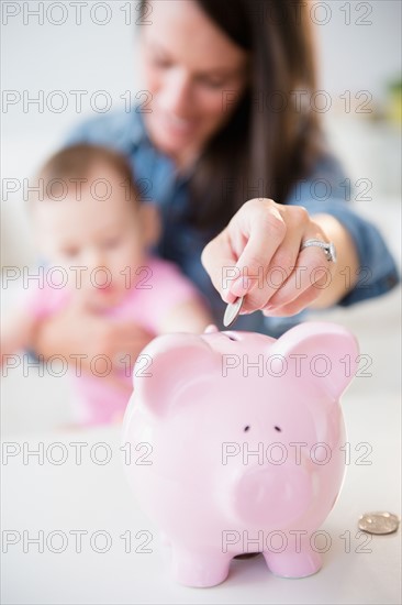 Mother with daughter (6-11 months) putting coins into piggybank