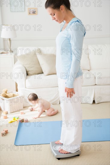Mother with daughter (6-11 months) exercising and checking weight in living room