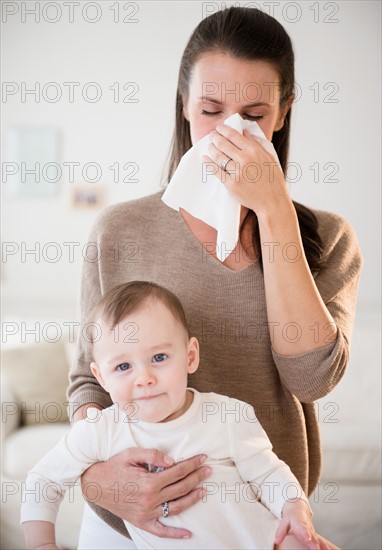 Mother holding her daughter (6-11 months) and blowing nose