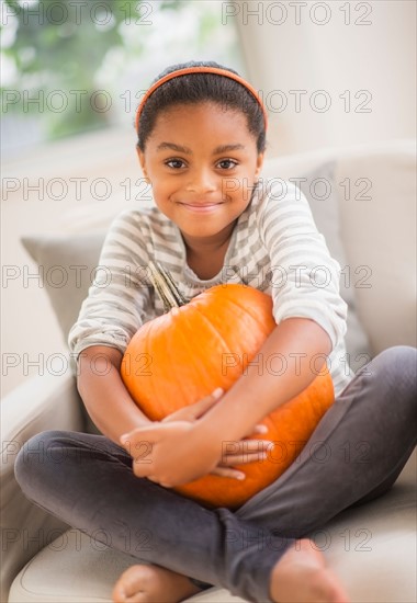 Portrait of smiling girl (6-7) sitting on sofa with pumpkin