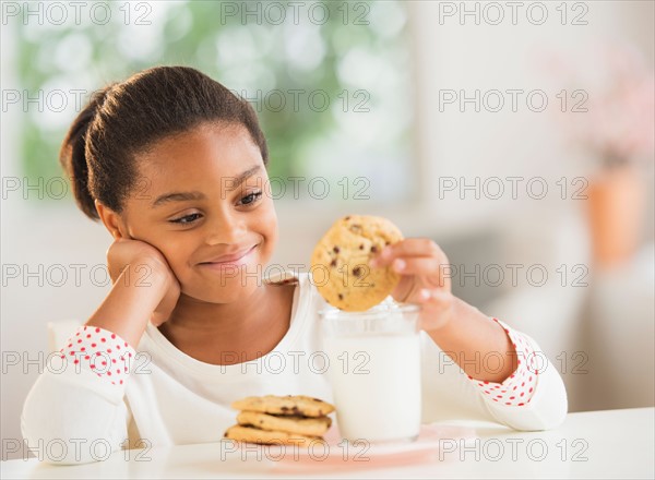 Girl (6-7) having cookie and milk