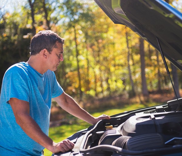 Man leaning on car with hood open at roadside